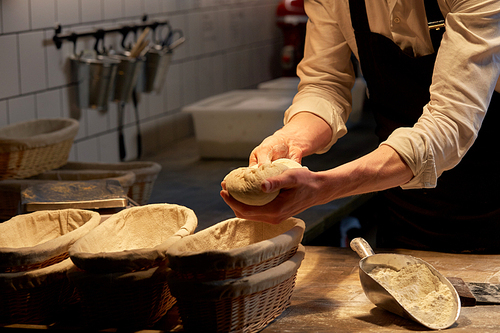 food cooking, baking and people concept - chef or baker putting yeast bread dough into baskets for rising at bakery kitchen