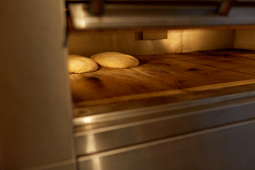 food, cooking and baking concept - yeast bread dough in oven at bakery kitchen