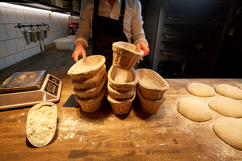 food cooking, baking and people concept - chef or baker preparing baskets while dough rising at bakery kitchen