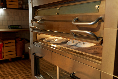 food, cooking and baking concept - yeast bread dough in oven at bakery kitchen