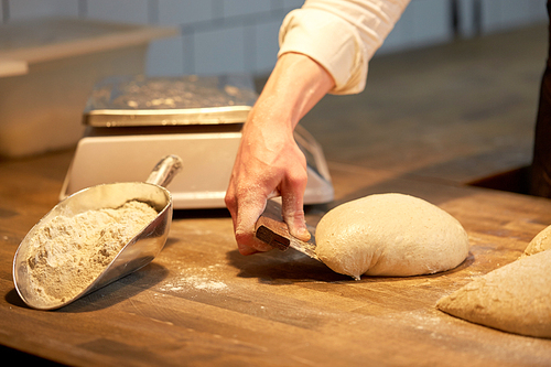 food cooking, baking and people concept - chef or baker portioning dough with bench cutter at bakery