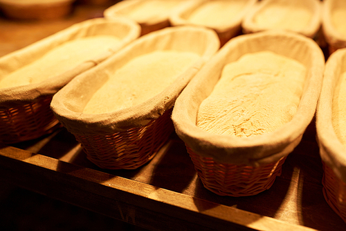 food, cooking and baking concept - yeast bread dough rising in baskets at bakery kitchen