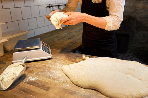 food cooking, baking and people concept - chef or baker portioning dough with bench cutter at bakery