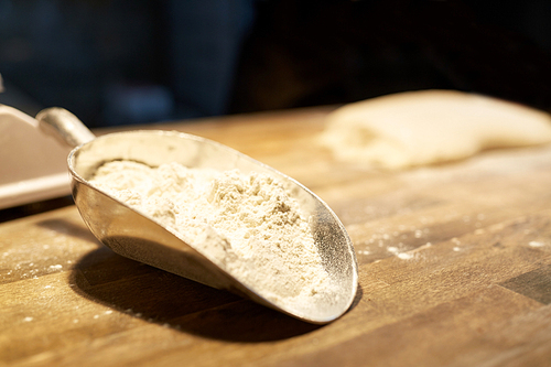 food, cooking and baking concept - flour in bakery scoop on wooden kitchen table