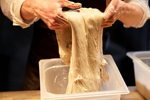 food cooking, baking and people concept - close up of baker hands kneading dough and making bread at bakery