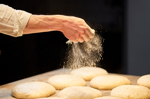 food cooking, baking and people concept - chef or baker making bread and pouring flour to dough at bakery