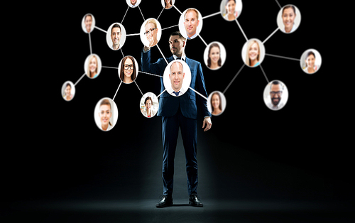 business, people and technology concept - businessman in suit with virtual icons of corporate network over black background