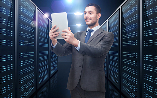 business, people and technology concept - happy smiling businessman in suit holding tablet pc computer over futuristic server room background