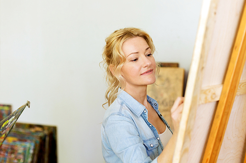 art school, creativity and people concept - woman with easel drawing at studio