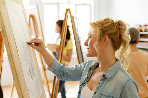 art school, creativity and people concept - woman with easel drawing at studio