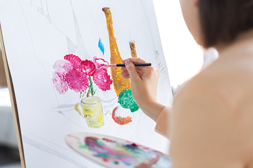 art, creativity and people concept - close up of artist with paint brush and easel painting still life on paper at studio