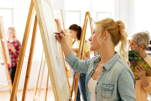 art school, creativity and people concept - woman with easel drawing at studio