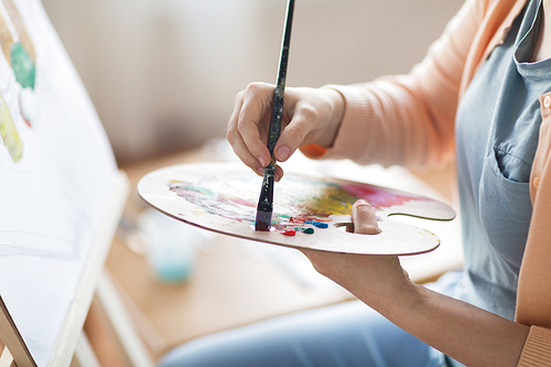 art, creativity and people concept - close up of artist with palette and brush painting still life on paper at studio