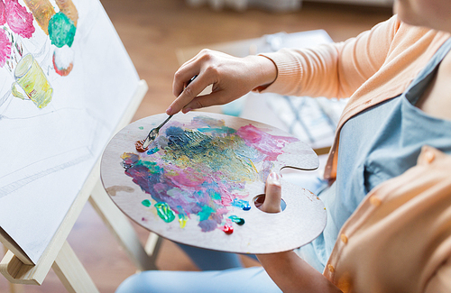 art, creativity and people concept - artist woman with palette knife and painting still life on easel at studio