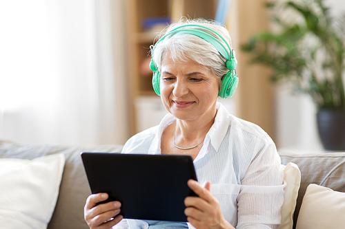 technology, people and lifestyle concept - happy senior woman in headphones and tablet pc computer listening to music at home