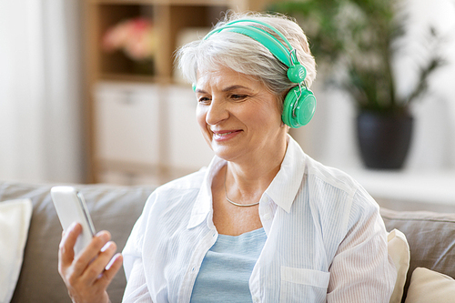 technology, people and lifestyle concept - happy senior woman in headphones and smartphone listening to music at home