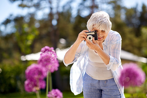 photography, leisure and people concept - happy senior woman with camera photographing flowers blooming at summer garden