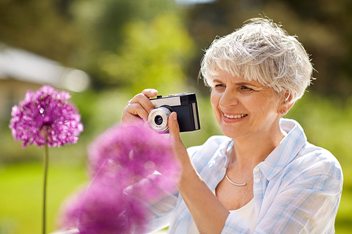 photography, leisure and people concept - happy senior woman with camera photographing flowers blooming at summer garden