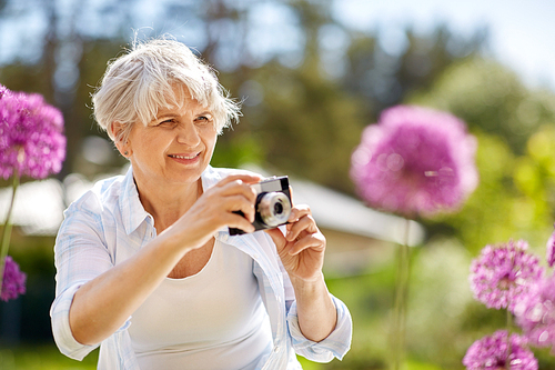 photography, leisure and people concept - happy senior woman with camera photographing flowers blooming at summer garden