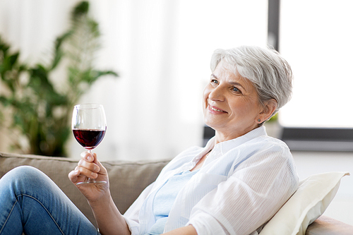 people, alcohol and leisure concept - happy smiling senior woman with glass of red wine at home