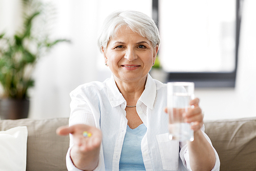age, medicine, healthcare and people concept - senior woman with pills and glass of water at home