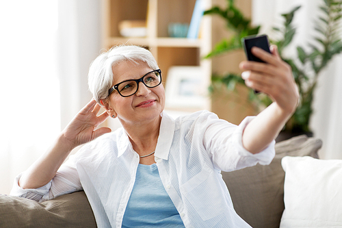 technology, communication and people concept - happy senior woman taking selfie by smartphone at home