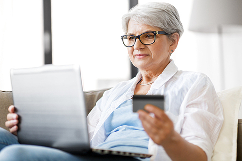 technology, online shopping and people concept - happy senior woman in glasses with laptop computer and credit or bank card at home
