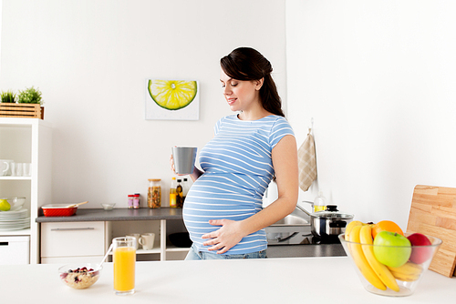 pregnancy, people and healthy eating concept - happy pregnant woman with cup of tea and food having breakfast at home kitchen