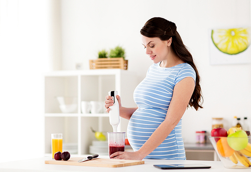 healthy eating, cooking, pregnancy and people concept - pregnant woman with blender preparing fruit smoothie drink at home kitchen