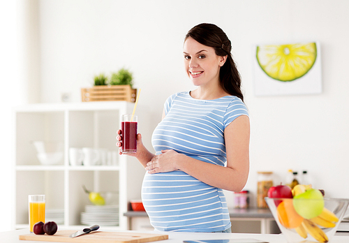 pregnancy, people and healthy eating concept - happy smiling pregnant woman drinking juice or smoothie at home kitchen