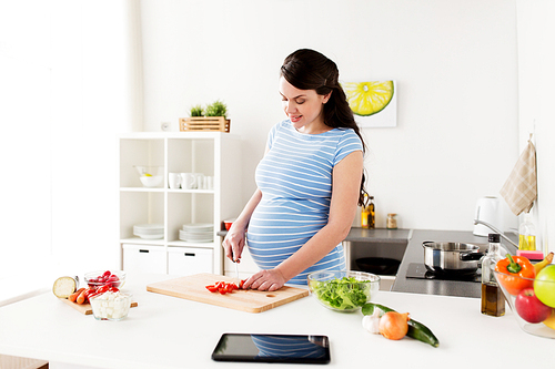 healthy eating, pregnancy and people concept - pregnant woman cooking and chopping cherry tomatoes at home kitchen
