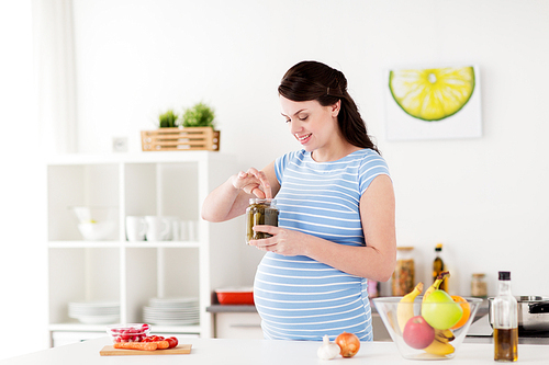 pregnancy, nutrition and people concept - happy pregnant woman eating pickles at home kitchen
