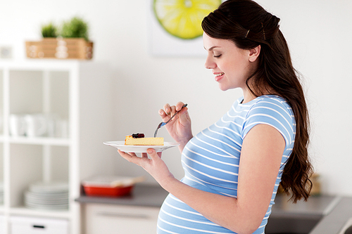 pregnancy, people and junk food concept - happy pregnant woman eating cake at home kitchen