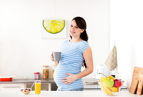 pregnancy, people and healthy eating concept - happy pregnant woman with cup of tea and food having breakfast at home kitchen