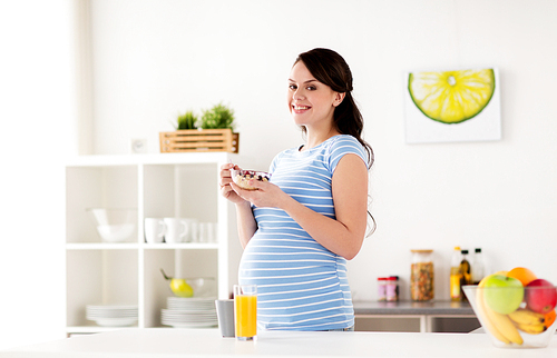 pregnancy, people and healthy eating concept - happy pregnant woman with muesli for breakfast at home kitchen