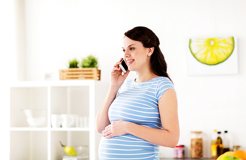 pregnancy, people and healthy eating concept - happy pregnant woman calling on smartphone at home kitchen