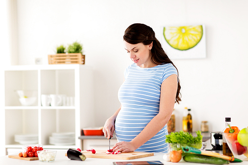 healthy eating, pregnancy and people concept - pregnant woman cooking and chopping vegetable at home kitchen