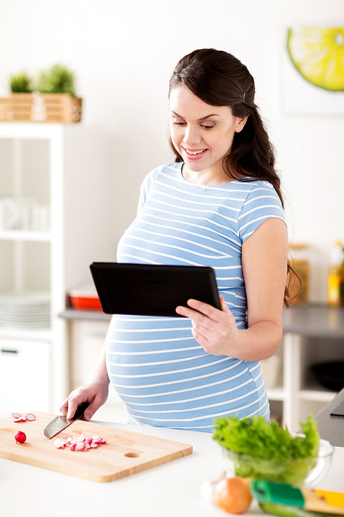 healthy eating, pregnancy and people concept - pregnant woman with tablet pc computer cooking vegetable salad at home kitchen