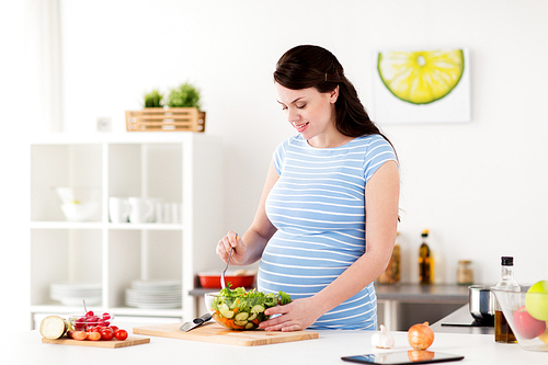 healthy eating, pregnancy and people concept - pregnant woman cooking vegetable salad at home kitchen