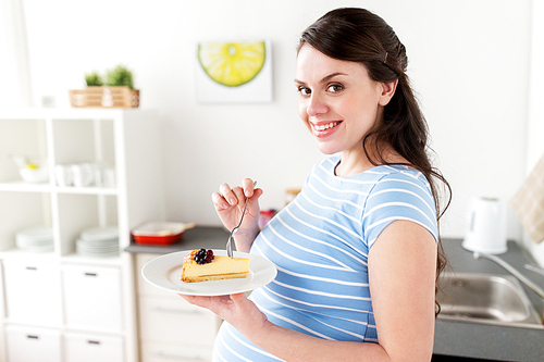 pregnancy, people and junk food concept - happy pregnant woman eating cake at home kitchen