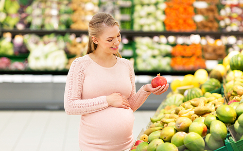 sale, shopping, food, pregnancy and people concept - happy pregnant woman with pomegranate at grocery store or supermarket