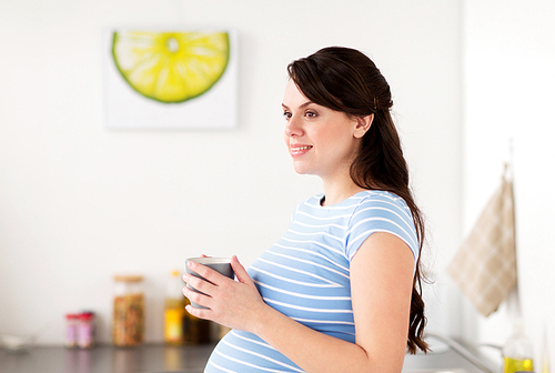 pregnancy, people and expectation concept - happy pregnant woman with cup of tea at home kitchen