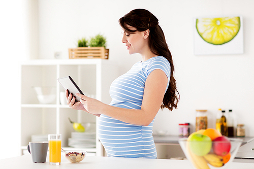 healthy eating, pregnancy and people concept - pregnant woman with tablet pc computer having breakfast at home kitchen
