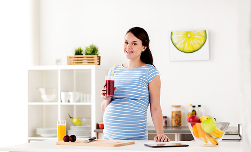 pregnancy, people and healthy eating concept - happy smiling pregnant woman drinking juice or smoothie at home kitchen