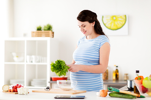 healthy eating, pregnancy and people concept - happy smiling pregnant woman with lettuce cooking vegetable salad at home kitchen