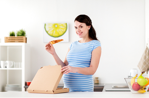 pregnancy, people and junk food concept - happy pregnant woman eating pizza at home kitchen