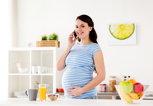 pregnancy, people and healthy eating concept - happy pregnant woman calling on smartphone and having breakfast at home kitchen