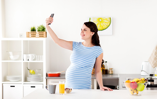 pregnancy, people and technology concept - happy pregnant woman with smartphone taking selfie and having breakfast at home kitchen