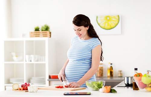 healthy eating, pregnancy and people concept - pregnant woman cooking vegetable salad and chopping cherry tomatoes at home kitchen