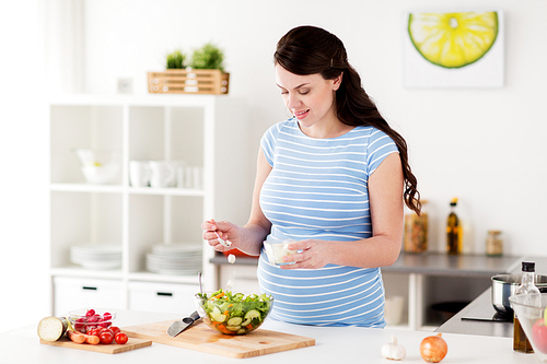 healthy eating, pregnancy, food and people concept - pregnant woman cooking vegetable salad with feta cheese at home kitchen